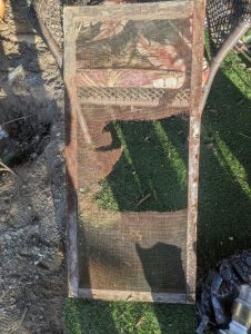 Photo of a wooden frame with a screen stapled to it. The screen is heavily rusted with gigantic holes in it