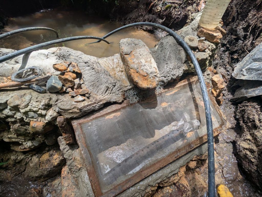 Photo of a rock-and-cement weir with a doubled-over extension of chicken wire jutting out of the weir opening, creating a "lip" that extends the length of the weir opening